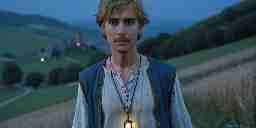 Young British wearing a glowing amulet walks through the English countryside at dusk.