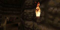 A low-poly flickering flaming torch on the wall of a cavern. A screenshot from Quake.